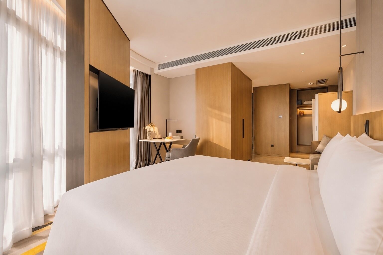 A hotel room with a large bed, a desk with a chair, a TV, and a wardrobe.