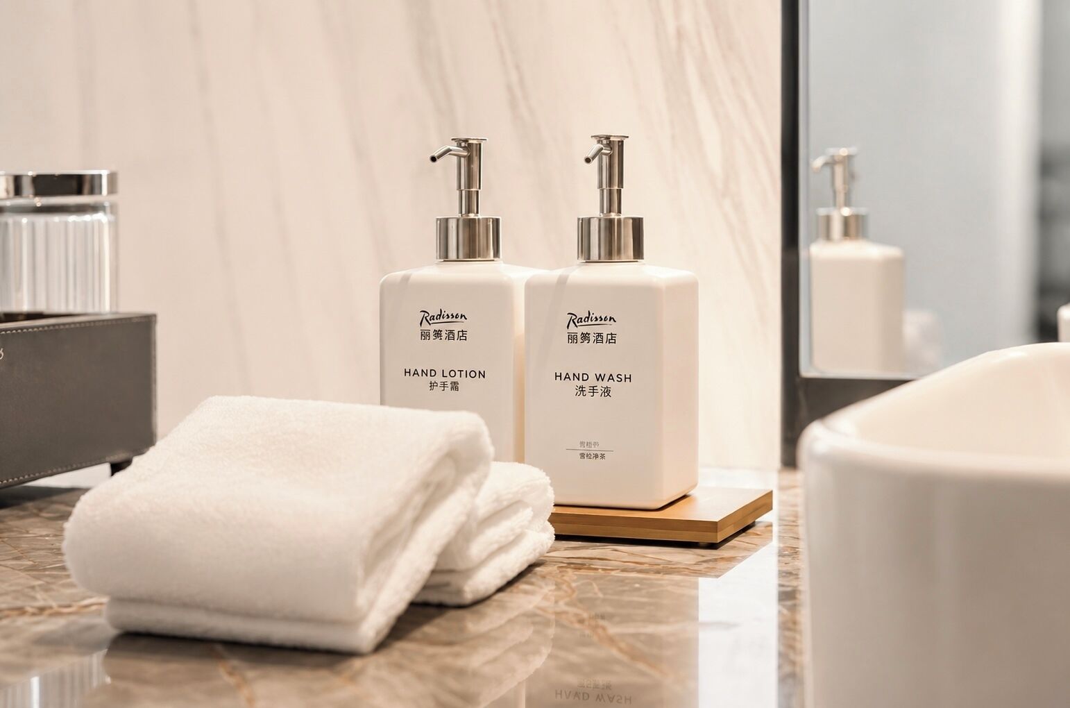 Een badkamer met een marmeren aanrecht, twee dispensers voor handlotion en handzeep, een opgevouwen witte handdoek en een spiegel.