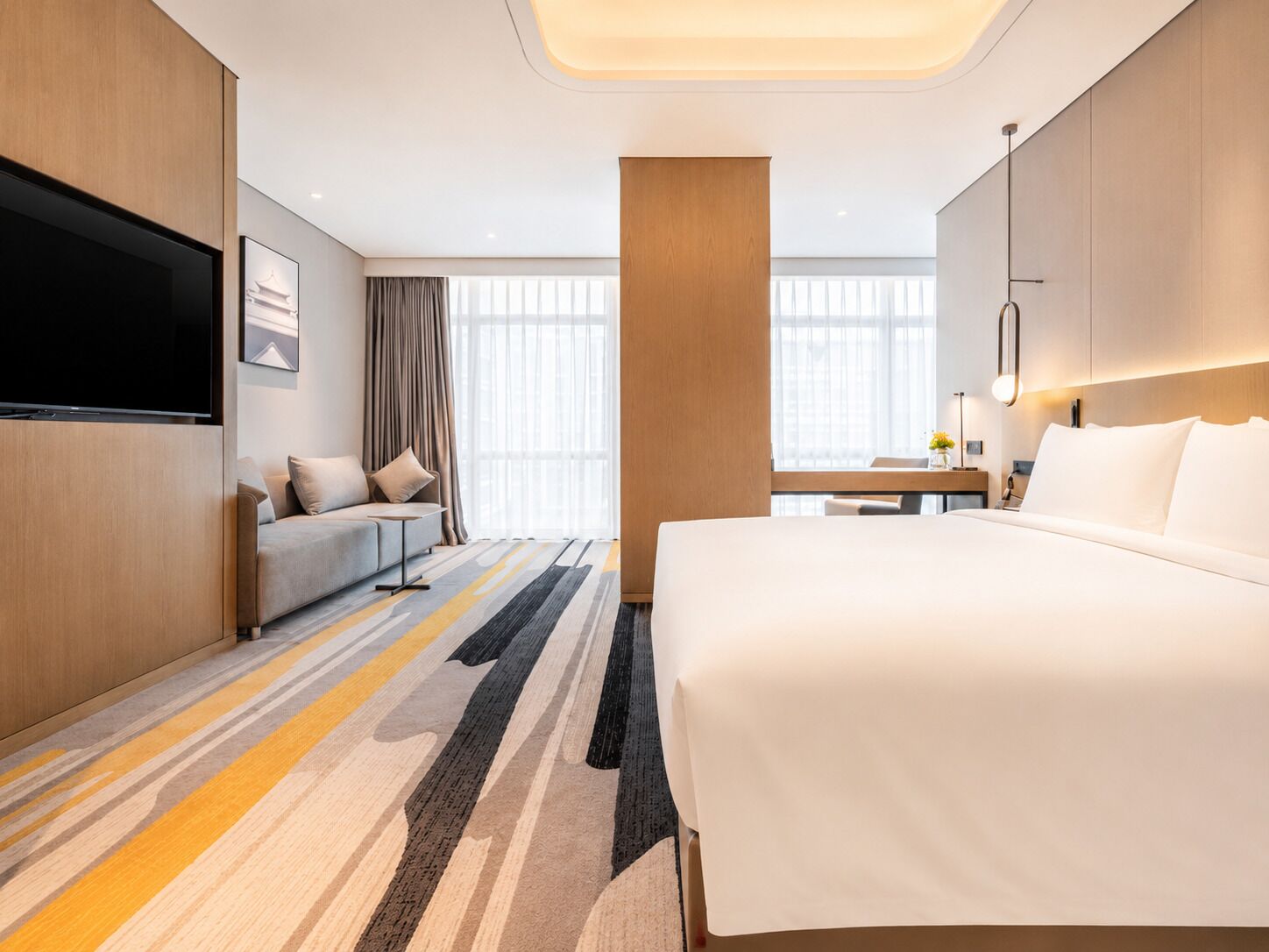 A hotel room with a bed, a sofa, a TV, and a desk with a lamp.