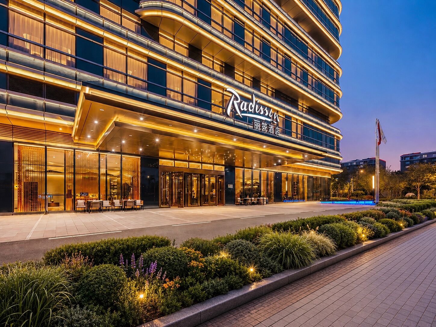 Um hotel moderno com fachada curva, grandes janelas de vidro e entrada bem iluminada.