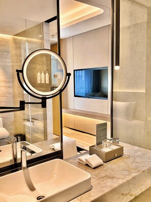 A modern bathroom with a large mirror, a sink, a vanity, and a television mounted on the wall. - Radisson Hotel, Beijing Daxing Airport     (Daxing)