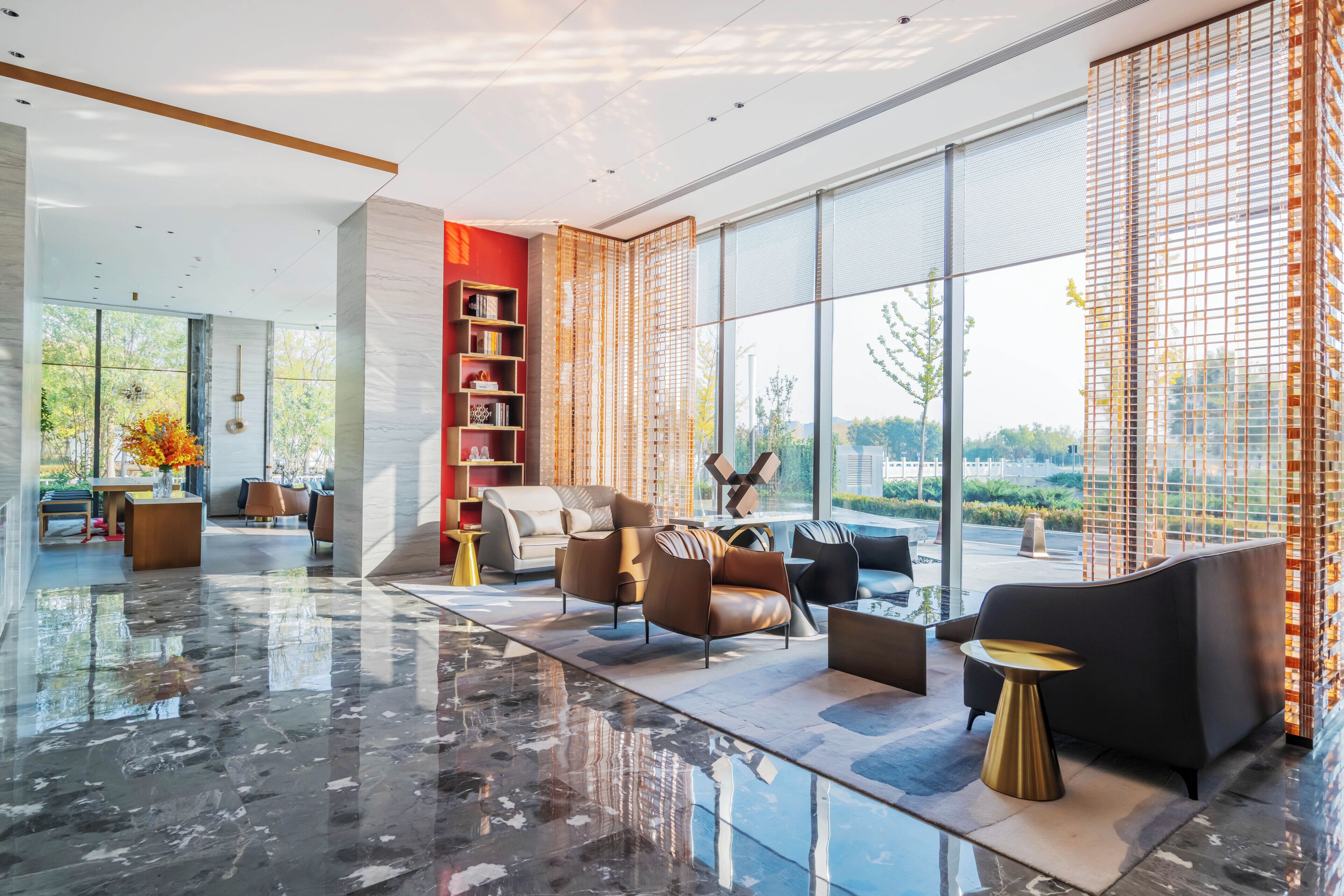 A modern lobby with a marble floor, leather sofas, a bookshelf, and large windows offering a view of the outdoors.
