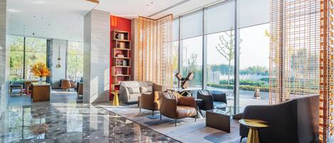 Eine moderne Lobby mit Marmorboden, Ledersofas, einem Bücherregal und großen Fenstern mit Blick ins Freie.