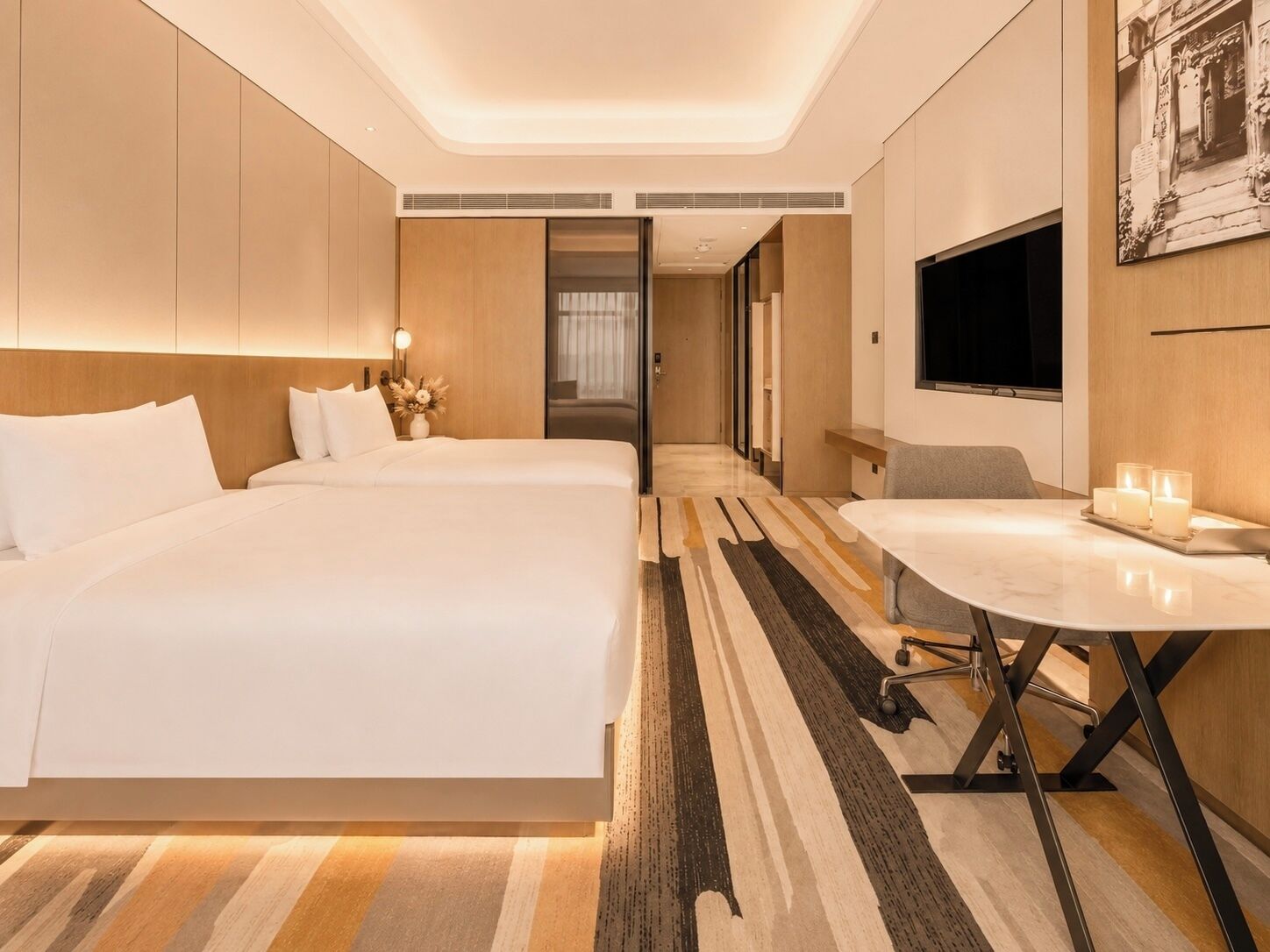 A hotel room with two beds, a dining table with candles, a TV, and a framed picture on the wall.
