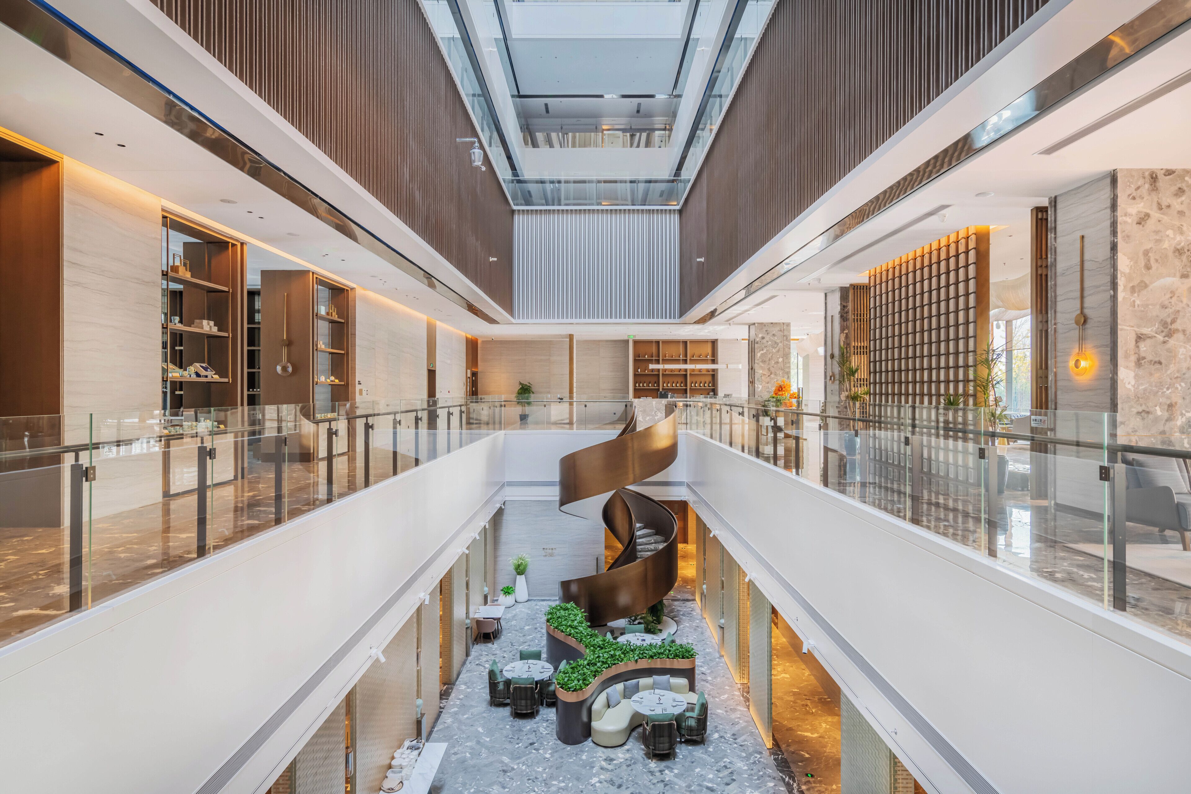 Un interior moderno con una escalera espiral central, barandillas de vidrio y un área de estar con plantas.
