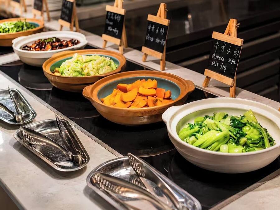 Monipuolinen buffet, jossa on tarjolla erilaisia ruokia, kuten wokkiruokia, kasviksia ja kulho keittoa.