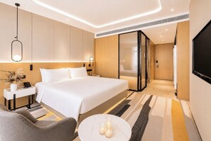 Quarto de hotel moderno com uma cama grande, mesas de cabeceira, uma TV e uma pequena área de estar.
