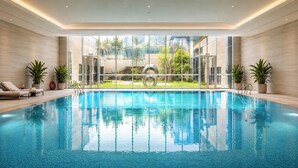A modern indoor swimming pool with clear glass walls, lounge chairs, and potted plants. - Radisson Hotel, Beijing Daxing Airport     (Daxing)