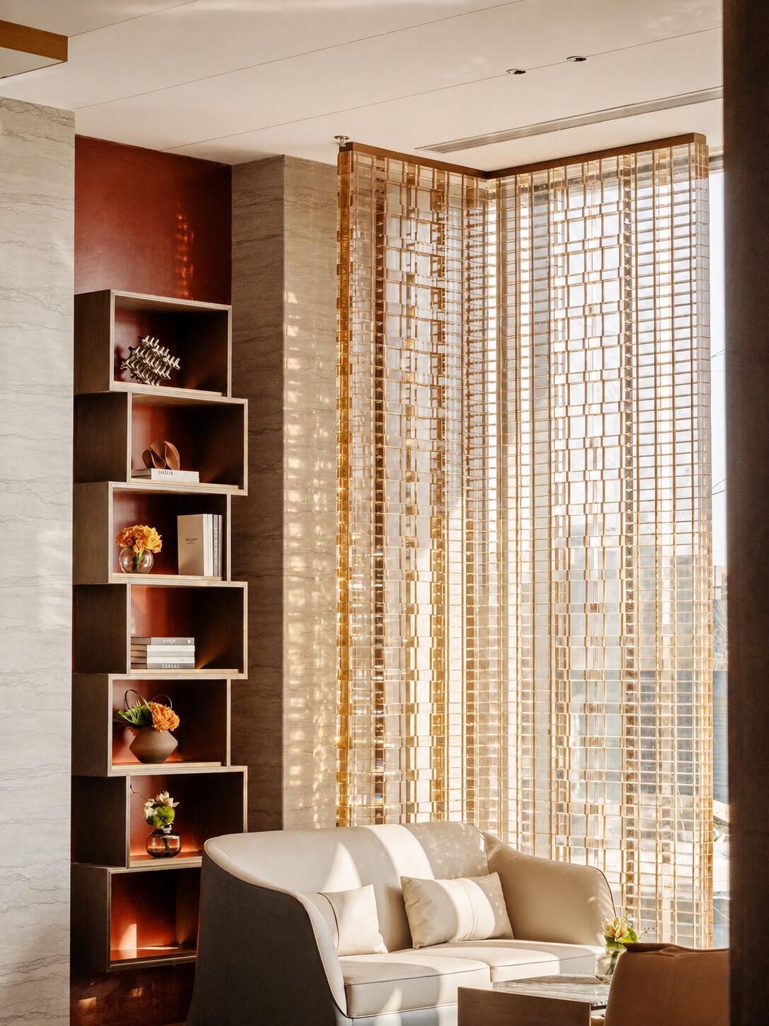 A modern living room with a sofa, a tall bookshelf, and a decorative curtain.
