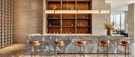 Una zona de bar con mostradores de mármol, taburetes de madera y estantes llenos de botellas.