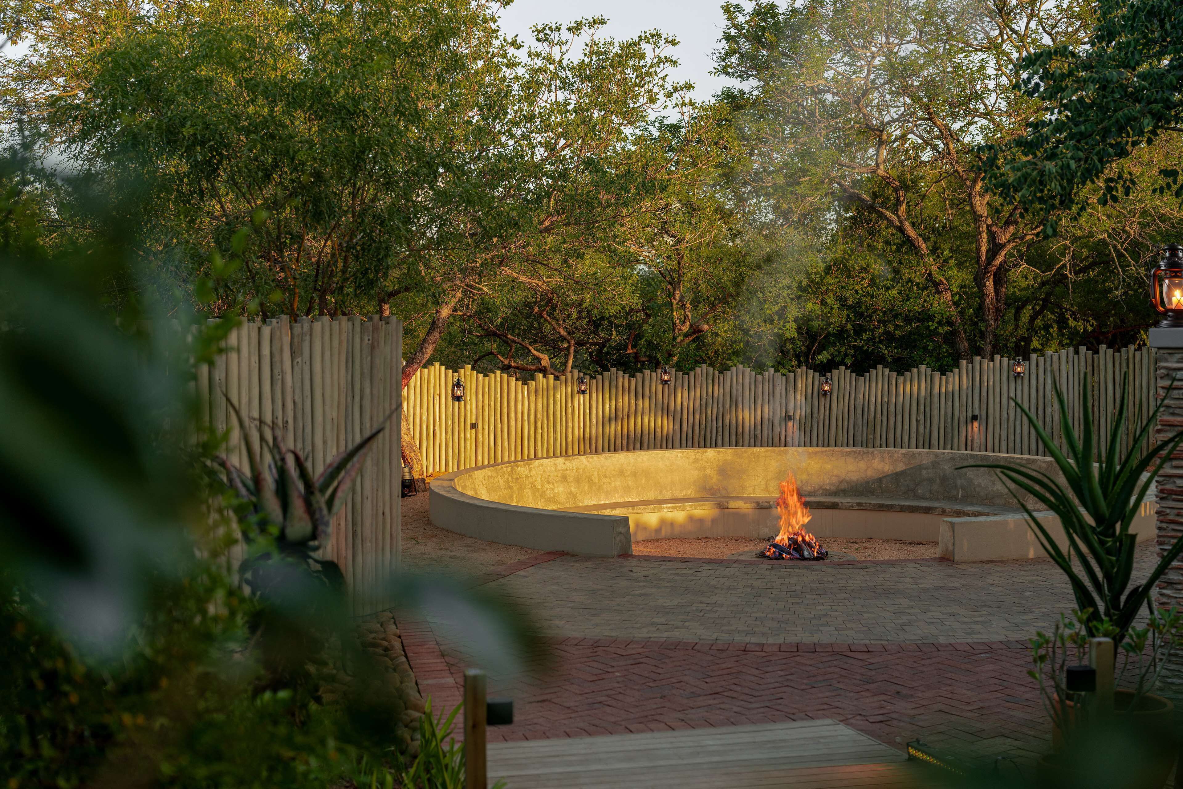 A circular outdoor seating area with a fire feature, surrounded by a wooden fence and trees.