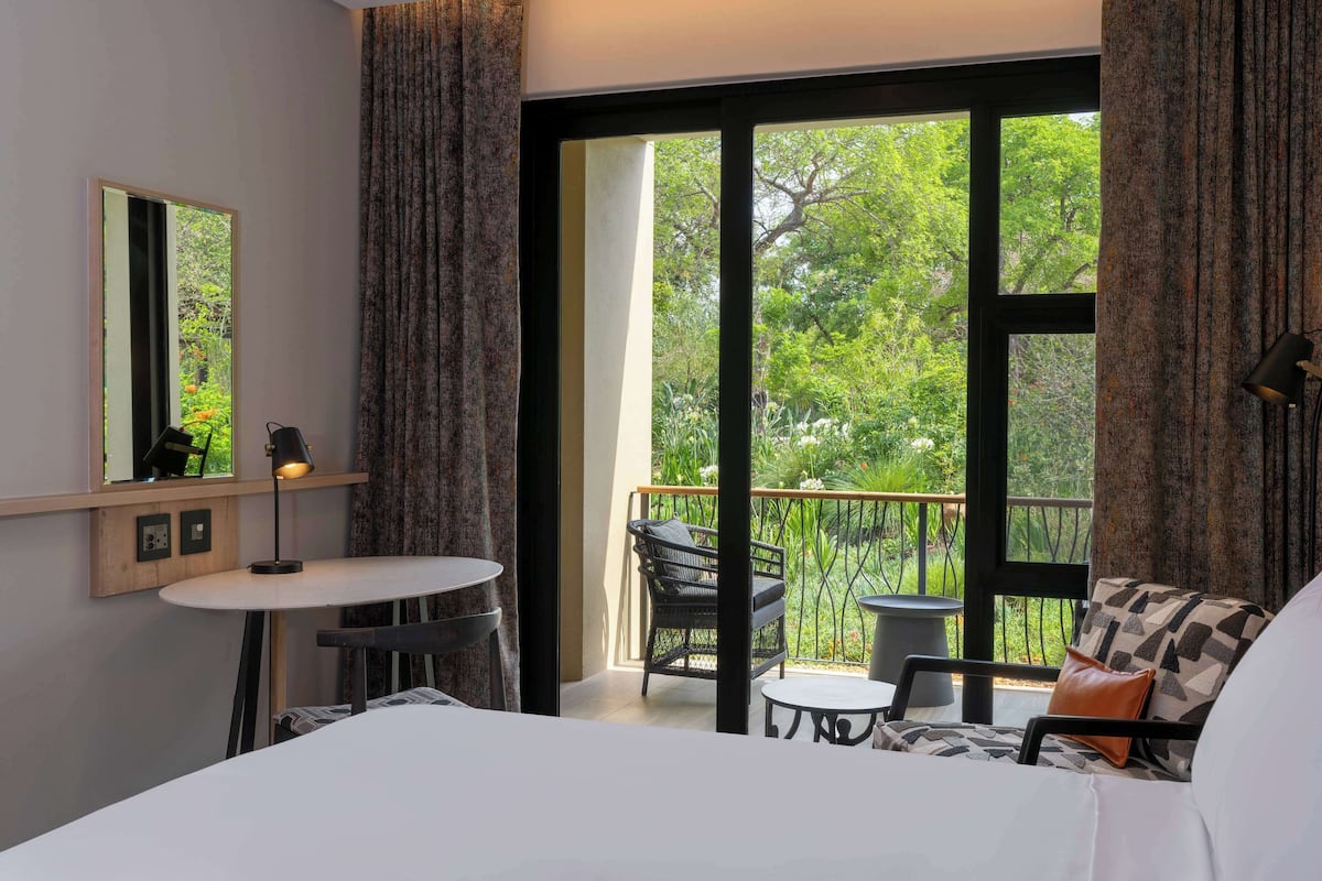 A bedroom with a large window, a bed, a small table, a chair, and a sofa.