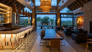 Un grand espace intérieur comprenant une longue table en bois, de nombreuses chaises, un coin bar et un espace détente avec des canapés et une cheminée.