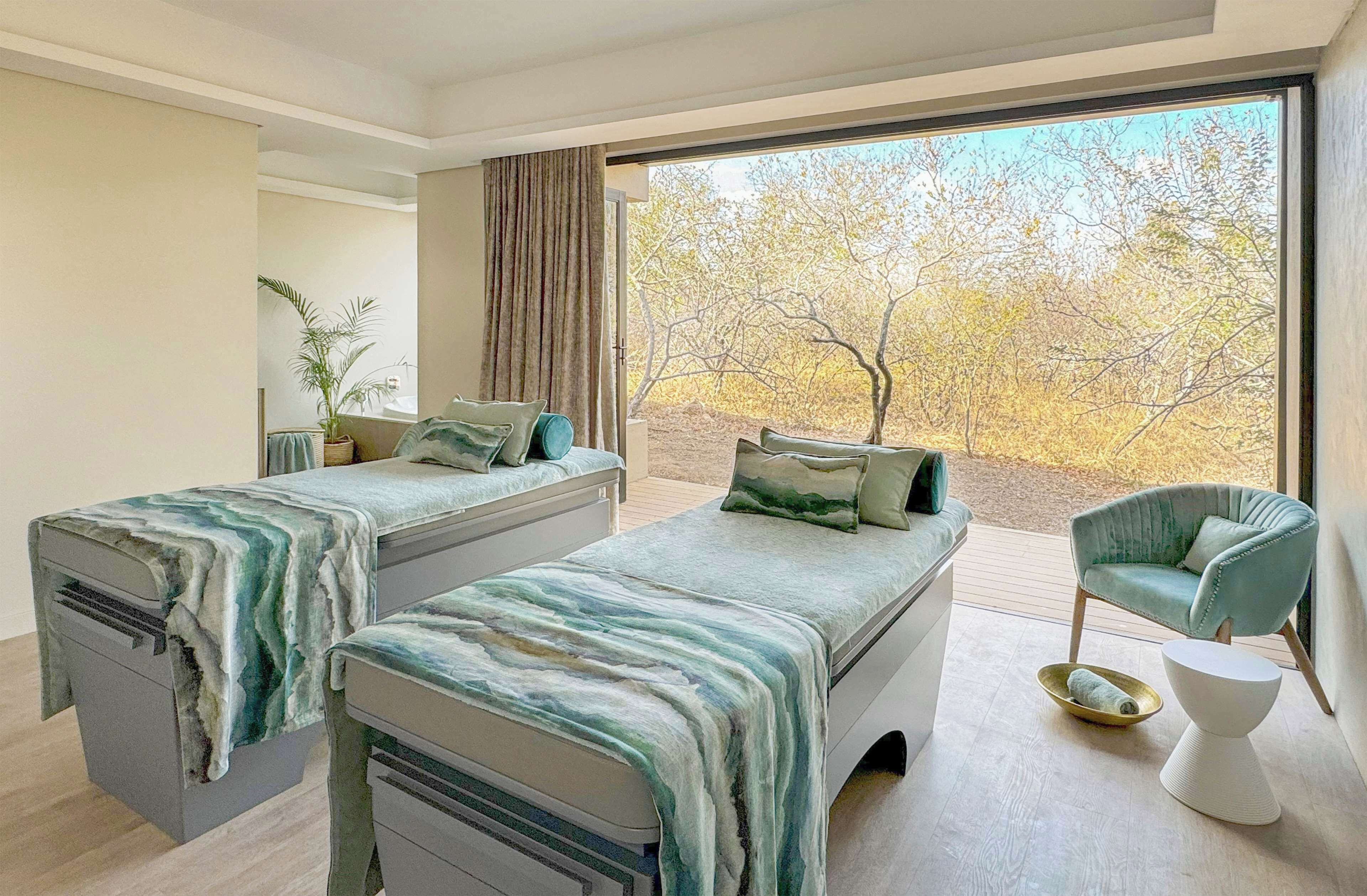 Un dormitorio moderno con dos camas, un ventanal grande y vistas a árboles.