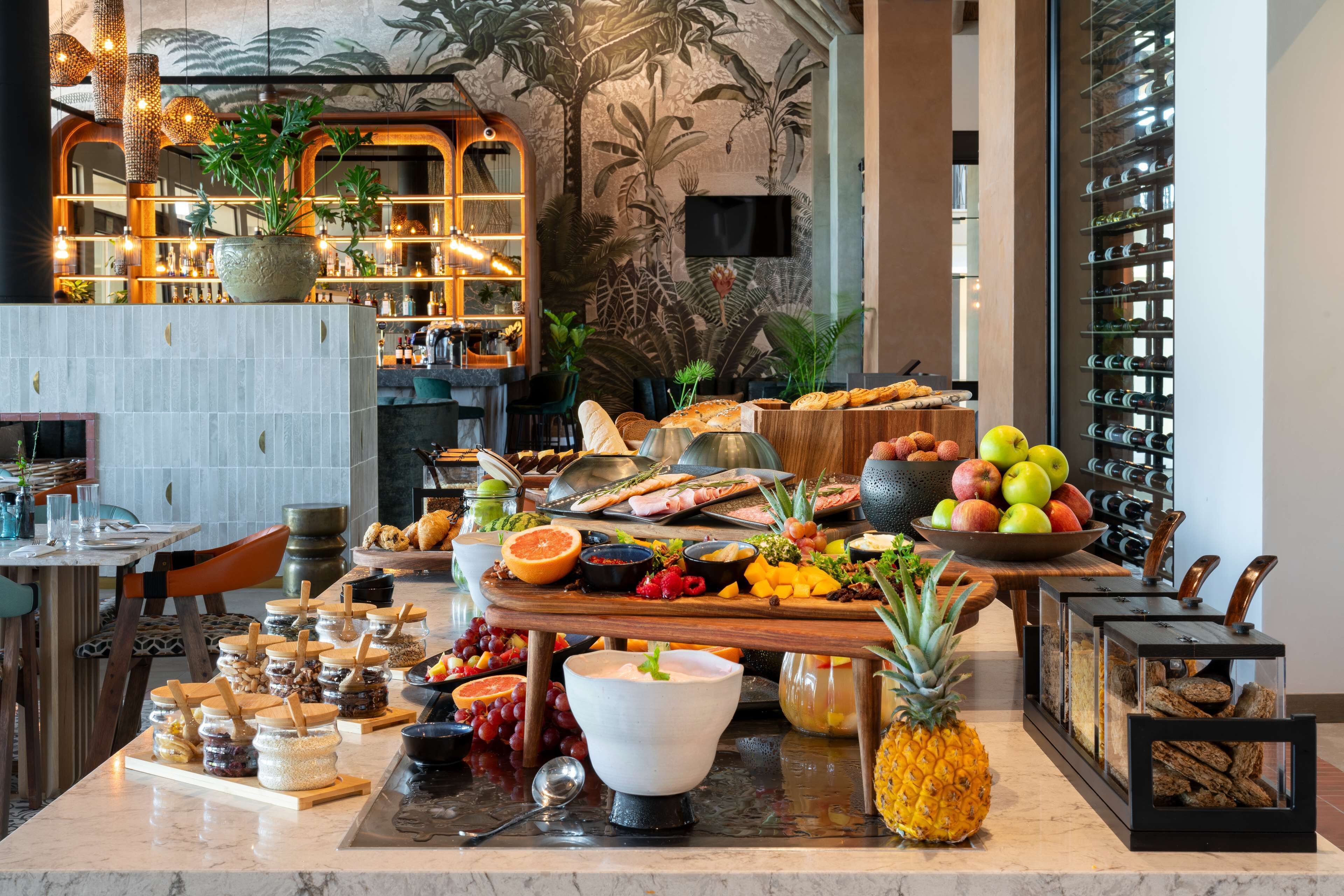 A buffet setup with various food items, a large bowl of fruits, and a pineapple centerpiece.