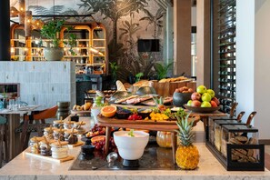 A buffet setup with various food items, a large bowl of fruits, and a pineapple centerpiece. - Radisson Safari Hotel Hoedspruit, A Verified Net Zero Hotel (Hoedspruit)