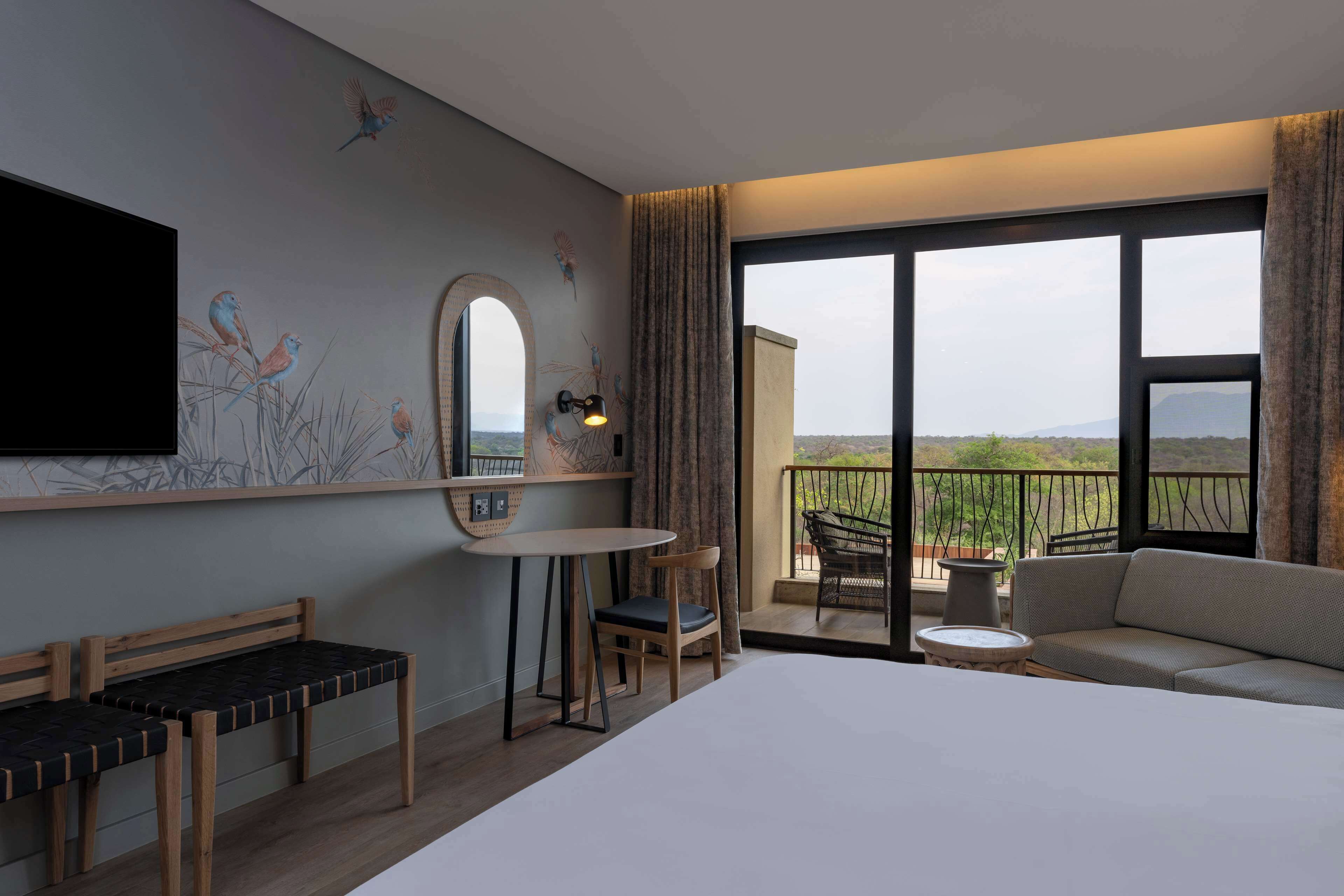 Habitación de hotel con cama, escritorio, silla, sofá y balcón con vistas.