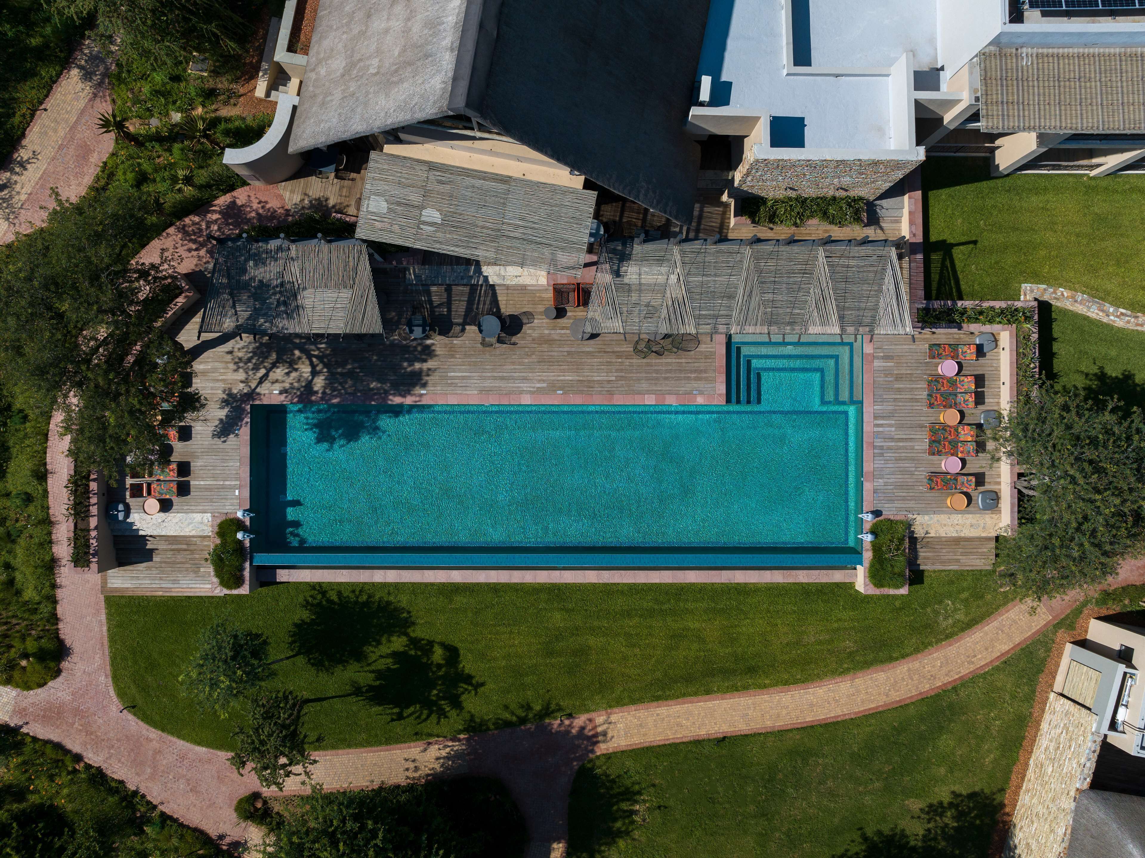 Eine Vogelperspektive zeigt ein Resort mit einem großen Schwimmbad, Sitzgelegenheiten im Freien und einem gepflegten Rasen.