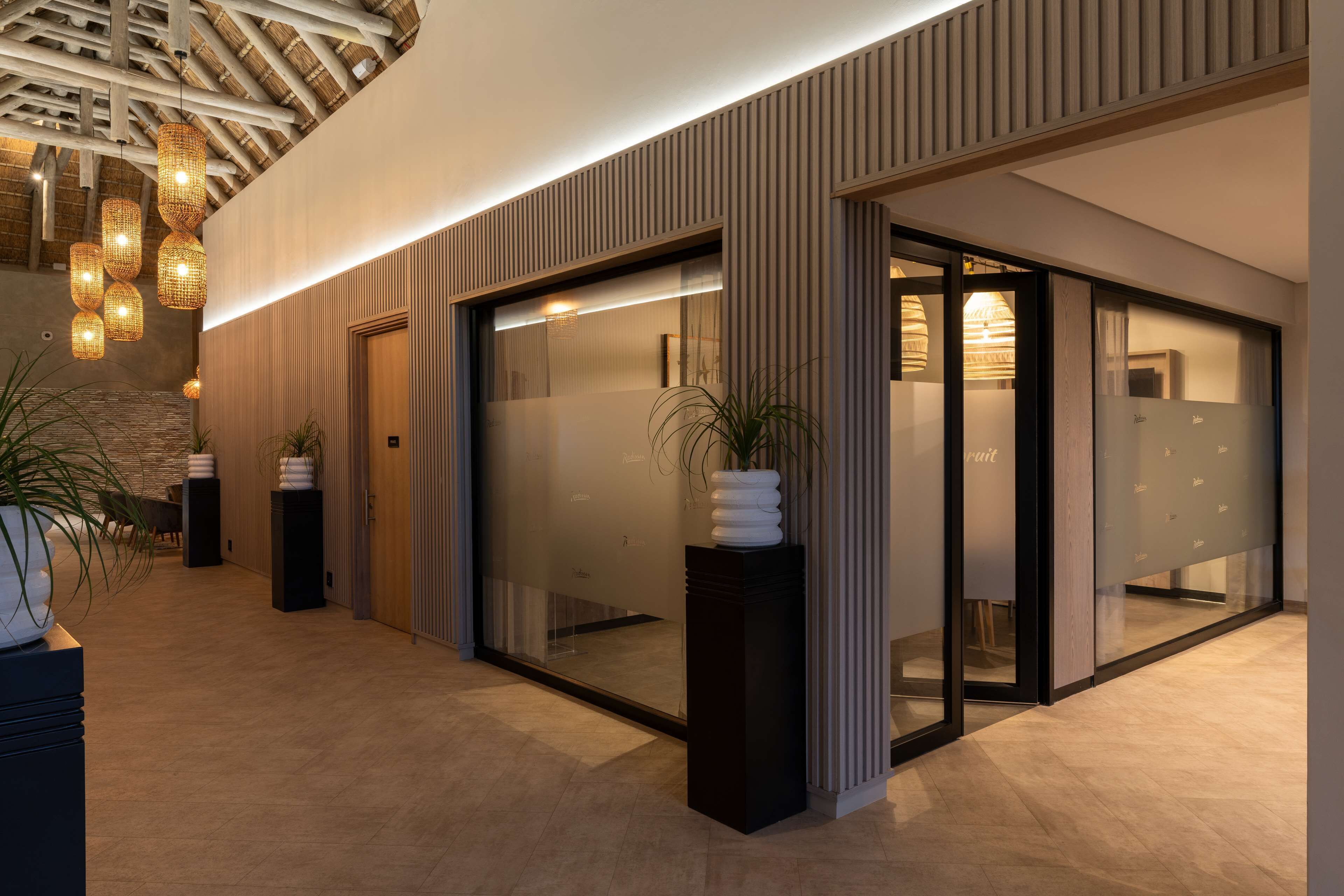 Een moderne hotel lobby met een houten plafond, glazen deuren en potplanten.
