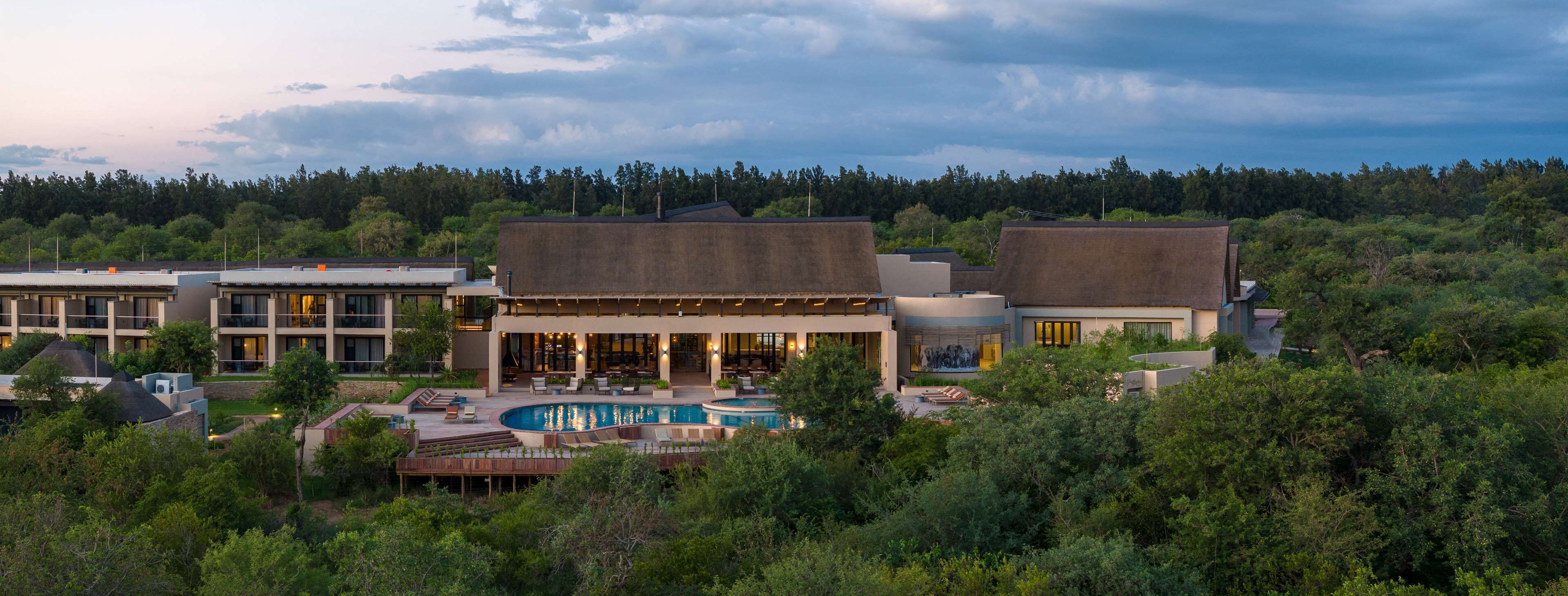 A resort with a swimming pool, multiple buildings, and a forested backdrop.