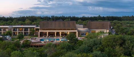 A resort with a swimming pool, multiple buildings, and a forested backdrop.