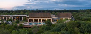 A resort with a swimming pool, multiple buildings, and a forested backdrop. - Radisson Safari Hotel Hoedspruit, A Verified Net Zero Hotel (Hoedspruit)