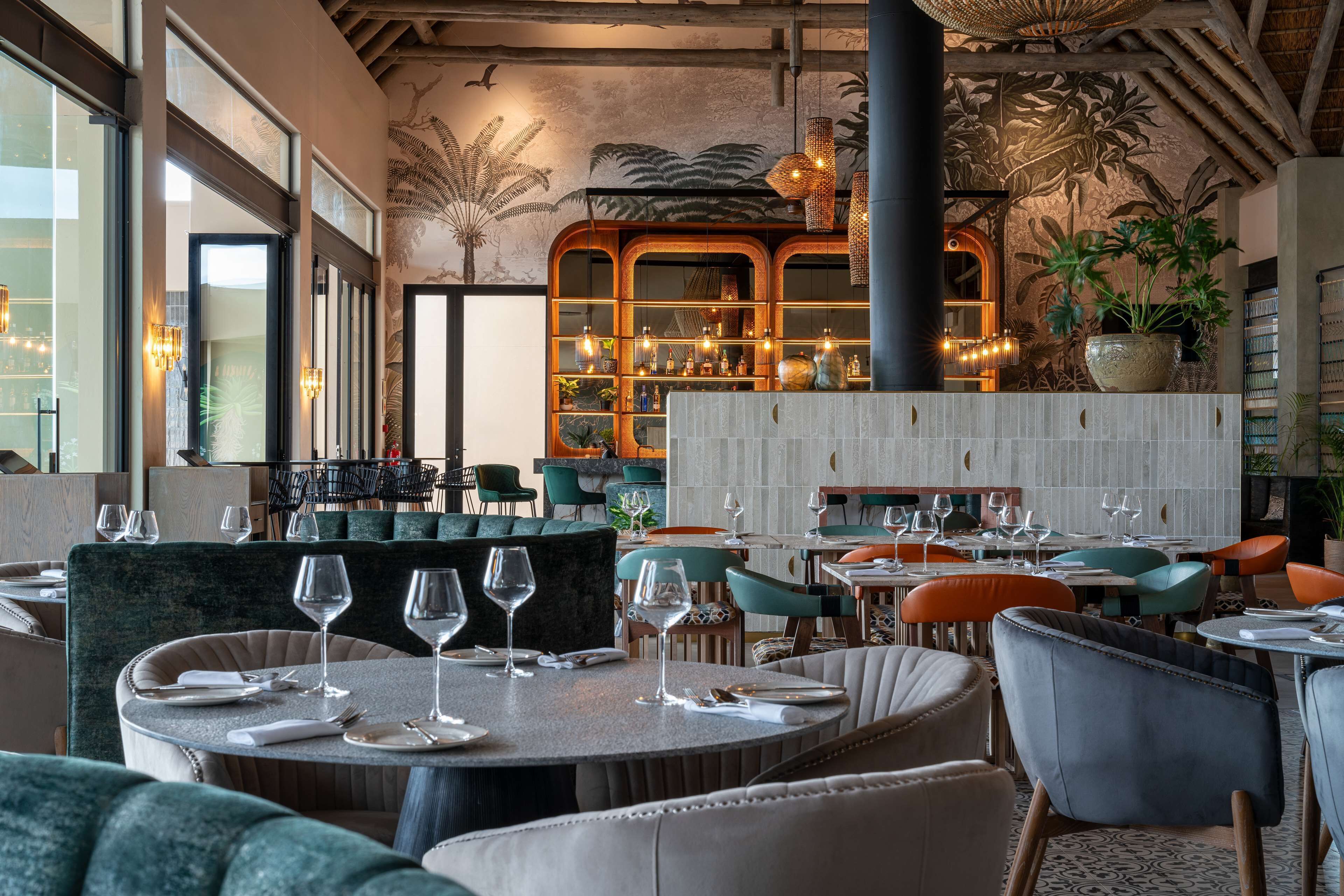 A restaurant with round tables, chairs, and a bar area with shelves of bottles.