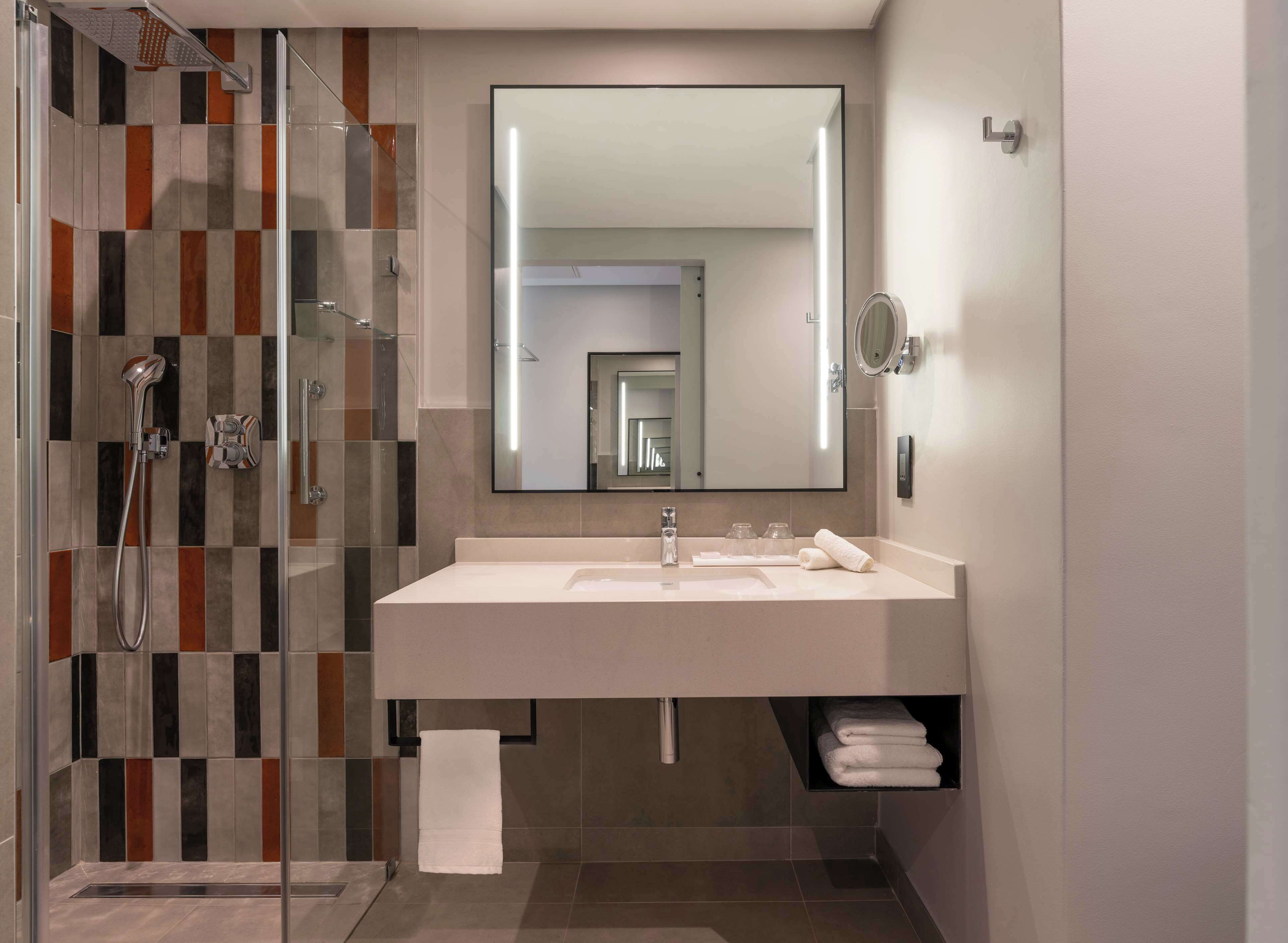 Une salle de bain moderne avec une douche à parois de verre, un grand miroir et un lavabo blanc.