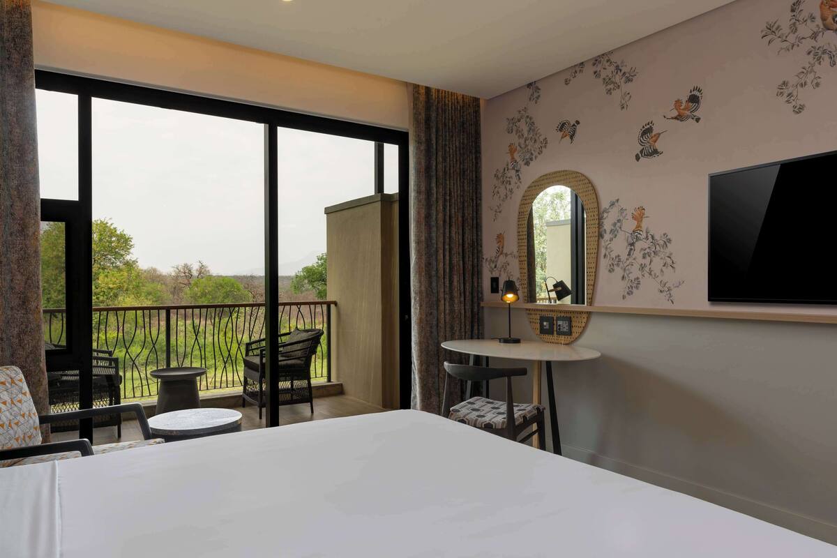 A hotel room with a balcony, a round table, a chair, a bed, and a TV mounted on the wall.