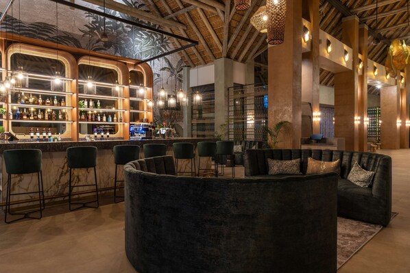 A bar area with a curved seating arrangement, bar stools, and a counter displaying various bottles. - Radisson Safari Hotel Hoedspruit, A Verified Net Zero Hotel (Hoedspruit)