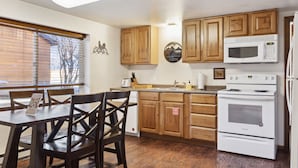 A kitchen with wooden cabinets, a microwave, an oven, and a dining table with chairs. - Outpost: Vine Street 3 - Close to Snow King (Jackson)