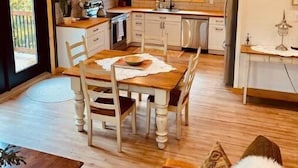 A cozy kitchen with wooden cabinets, a dining table, and a view of the outdoors. - Cozy Ski Retreat with Moutain View/Ski In Property/Hot tub/5 mins to the Lifts (Fernie)