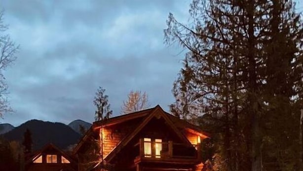 A wooden cabin with a porch, surrounded by trees and mountains. - Cozy Ski Retreat with Moutain View/Ski In Property/Hot tub/5 mins to the Lifts (Fernie)