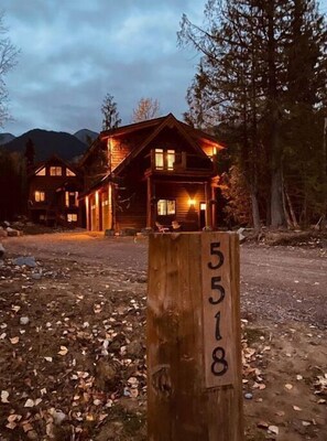 Una baita di legno con un portico, circondata da alberi e montagne.