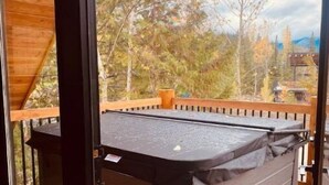 A hot tub on a wooden deck with a view of trees and mountains. - Cozy Ski Retreat with Moutain View/Ski In Property/Hot tub/5 mins to the Lifts (Fernie)