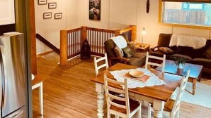 A spacious living area with a wooden dining table, chairs, a sofa, and a window. - Cozy Ski Retreat with Moutain View/Ski In Property/Hot tub/5 mins to the Lifts (Fernie)