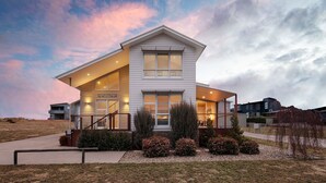 A modern two-story house with a large balcony, a covered entryway, and a sign indicating it is a retreat. - Alpine Snow Angels Retreat (Jindabyne)