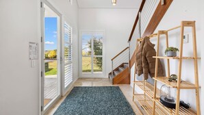 A hallway with a wooden staircase, a coat rack with a puffer jacket, and a small shelf with a plant and decorative items. - Alpine Snow Angels Retreat (Jindabyne)