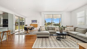 A spacious living area with a large sofa, a dining table, and a kitchen area with a built-in oven. - Alpine Snow Angels Retreat (Jindabyne)