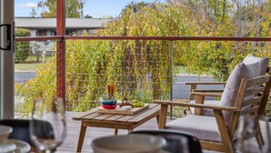 A wooden deck with a table and chairs, a view of a garden with a trellis and autumn foliage, and a building in the background. - Alpine Snow Angels Retreat (Jindabyne)
