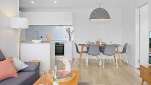 A modern kitchen with white cabinets, a dining area with a wooden table and chairs, and a grey pendant light.