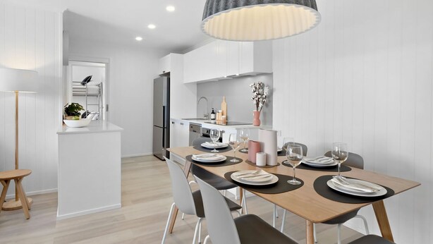 A modern kitchen with white cabinets, a wooden dining table set with plates and glasses, and a pendant light above.