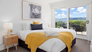 A bedroom with a bed, a nightstand, a window with a view, and a framed picture on the wall.