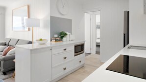 A modern kitchen with white cabinetry, a microwave, and a bowl of fruit on the counter.
