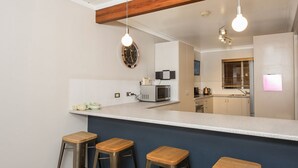 A modern kitchen with a bar area, wooden stools, a microwave, and a clock on the wall. - Erulisse (Jindabyne)