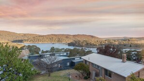 A modern house with a large backyard, a view of a lake, and surrounding hills. - Erulisse (Jindabyne)