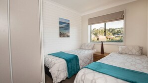 A bedroom with two beds, a window with a view of greenery and a bridge, and a painting on the wall. - Erulisse (Jindabyne)