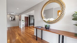 Un couloir moderne avec un plancher en bois, un grand miroir décoratif, une plante en pot et un tableau encadré accroché au mur.