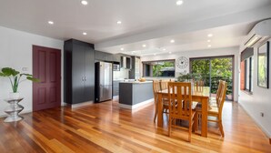Une cuisine moderne avec des meubles de couleur sombre, un îlot central et un coin repas doté de chaises en bois.