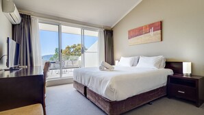 Ein Hotelzimmer mit einem großen Bett, einem Schreibtisch, einem Flachbildfernseher, einem Sessel und Blick ins Freie.
